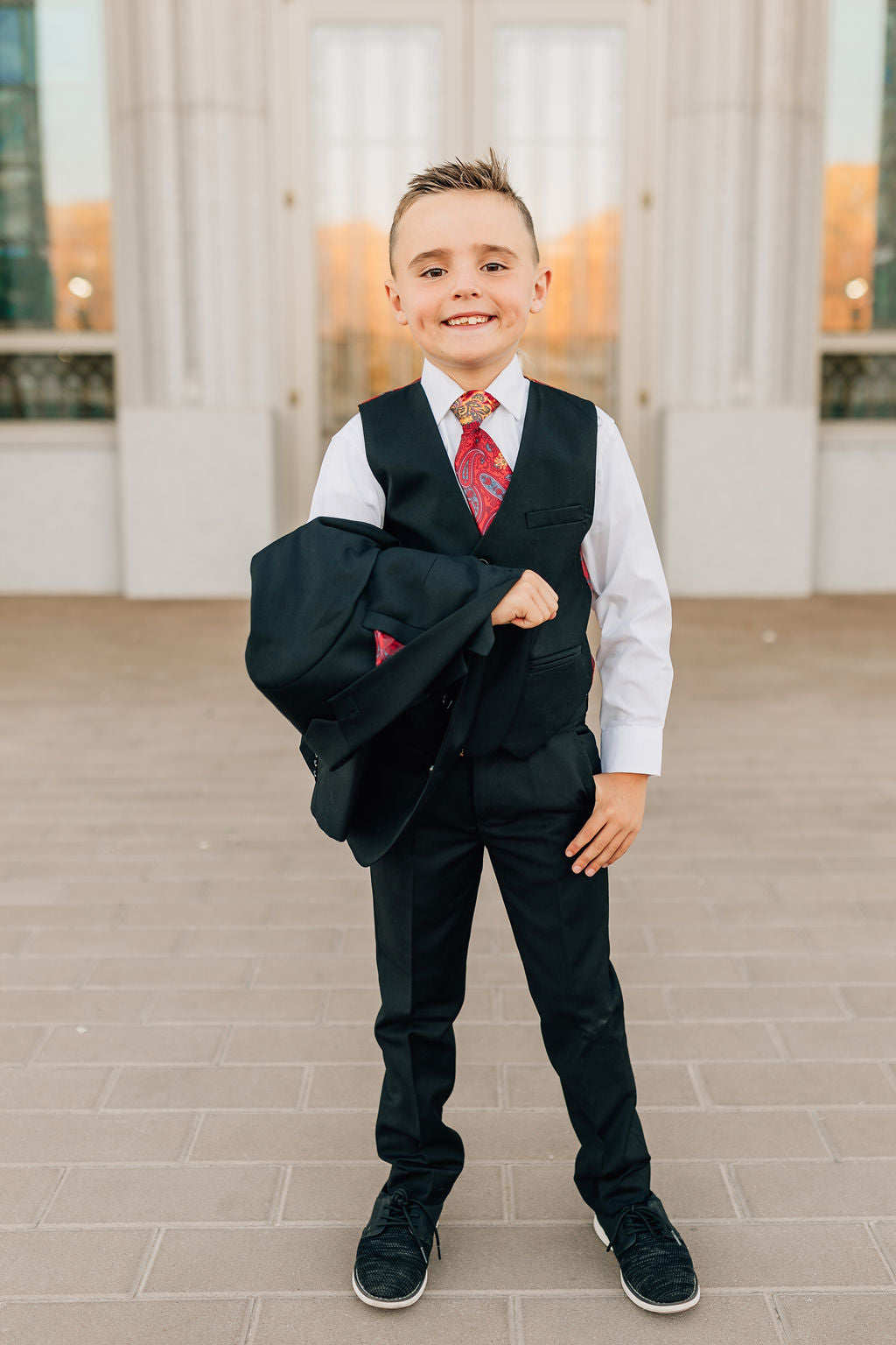 boy in black suit with jacket over arms